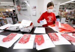 In this May 5, 2020 photo, University of Wisconsin Bookstore worker Stephanie Blaser packages GPA honor stoles purchased by UW-Madison graduates at the store's State Street location in Madison, Wis.