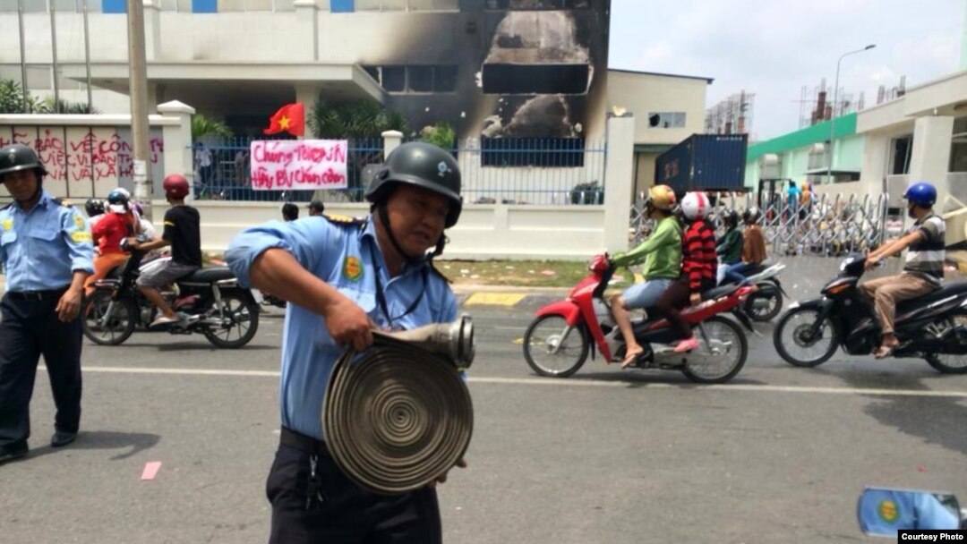 Một nhà máy ở Bình Dương bị đốt. Phía trước là biểu ngữ với hàng chữ 'Chúng tôi yêu Việt Nam. Hãy bảo vệ chén cơm."