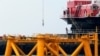  Trabajadores miran desde una barcaza de construcción junto la primera estructura de soporte de la chaqueta instalada para soportar una turbina para un parque eólico en aguas del océano Atlántico frente a Block Island, EE. UU., el 27 de julio de 2015. 