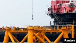  Trabajadores miran desde una barcaza de construcción junto la primera estructura de soporte de la chaqueta instalada para soportar una turbina para un parque eólico en aguas del océano Atlántico frente a Block Island, EE. UU., el 27 de julio de 2015. 