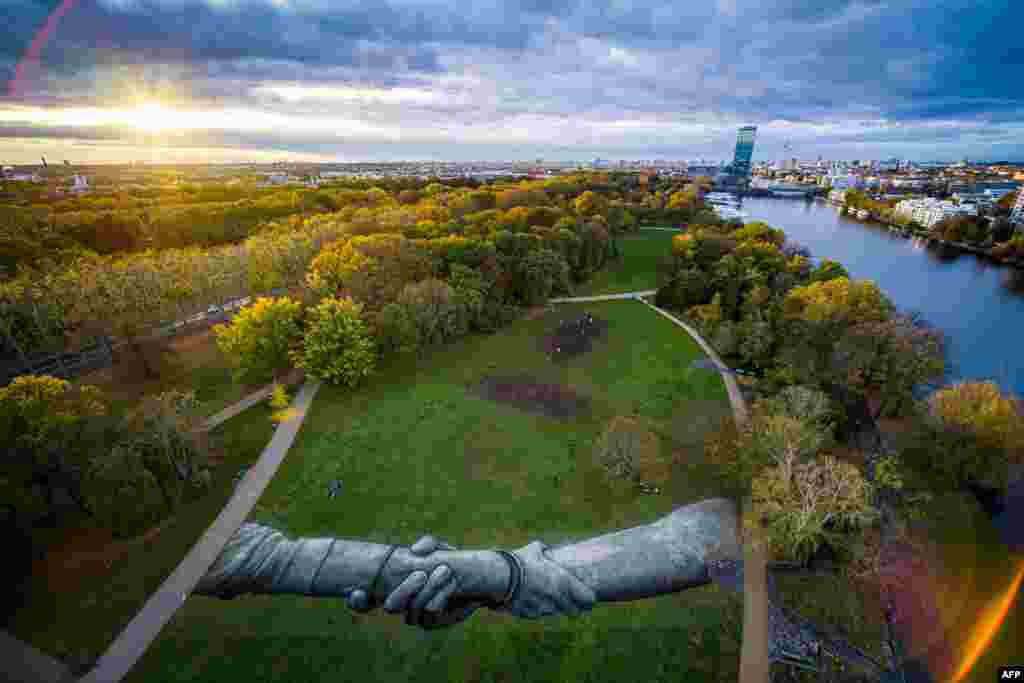 This handout picture released by Saype and Valentin Flauraud shows a giant biodegradable land art painting by French-Swiss artist Saype, representing two hands clasped together in the Treptower Park in Berlin, part of Saype&#39;s &quot;Beyond Walls&quot; project.