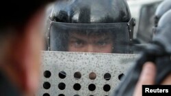 A police officer looks out from behind his shield as he and his colleagues block emergency workers as they protest against the draft state budget for 2014, near the Ukrainian parliament building in Kyiv, Jan. 14, 2014.