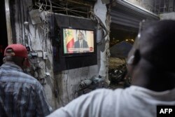 FILE —People watch the Senegal's President Macky Sall during a live press conference broadcast on the national television, in the district of Medina in Dakar on February 22, 2024.