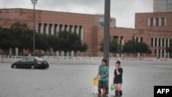 Grant Lu (L) dan Naomi Pringle berdiri di tempat parkir banjir di kampus Rice University di Houston, Texas yang terendam banjir air akibat hantaman badai tropis Harvey, 27 Agustus 2017. (Foto: Scott Olson/Getty Images/AFP).