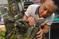 En esta imagen tomada el 5 de agosto de 2020, el artista de modelos en miniatura Leon Huang posa para una fotografía con su trabajo durante una entrevista en FM Dioramas en Taoyuan, norte de Taiwán.