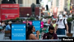 Seorang perempuan mengenakan masker sedang minum kopi di Times Square, di tengah pandemi virus corona, di New York, 5 Juli 2020. (Foto: Jeenah Moon/Reuters)