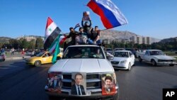 Des partisans du régime de Bachar al-Assad brandissent des drapeaux syriens, iraniens et russes en scandant des slogans contre le président américain Donald Trump, à Damas, le 14 avril 2018.