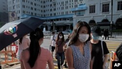 FILE - People wearing masks to protect against the coronavirus cross a street in Hong Kong, Aug. 20, 2020.