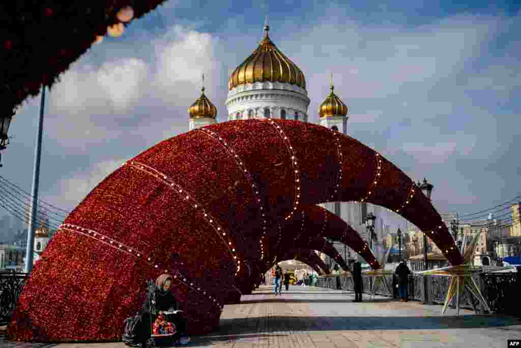An elderly woman sells traditional Russian wooden nesting dolls, called Matryoshka dolls, on a bridge over the Moskva River, in front of the Cathedral of Christ the Savior in downtown Moscow.