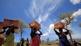 FILE - Women from the Dadinga tribe carry boxes of oil during food distribution by the World Food Program in the village of Lauro, Budy county, Eastern Equatoria state, South Sudan, April 3, 2010.