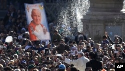 Le pape François passe devant une bannière représentant saint Jean-Paul II mentionnant en italien "meilleurs vœux", lors d’une audience publique sur la place Saint-Pierre au Vatican, le 22 octobre 2016. 