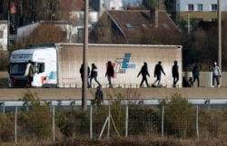 FILE - Migrants walk past a truck on the road that leads to the Channel Tunnel crossing in Calais, France, Dec.16, 2020.
