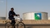 Seorang karyawan mengendarai sepeda melintas di depan tangki penyimpanan minyak di fasilitas milik Saudi Aramco di Abqaiq, Saudi Arabia.