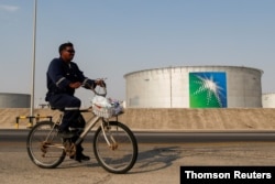 FILE - An employee rides a bicycle past oil tanks at the Saudi Aramco oil facility in Abqaiq, Saudi Arabia.