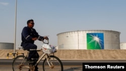 FILE - An employee rides a bicycle next to oil tanks at an Aramco oil facility in Abqaiq, Saudi Arabia, Oct. 12, 2019.