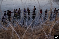 资料照片: 2023年9月23日德克萨斯州伊格尔帕斯: 移民穿过格兰德河从墨西哥进入美国后等待爬过六角形铁丝网
