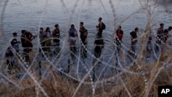 FILE - Migrants wait to climb over concertina wire after they crossed the Rio Grande and entered the U.S. from Mexico, Sept. 23, 2023, in Eagle Pass, Texas. An appeals court issued an order March 19, 2024, putting a controversial Texas border law back on hold.
