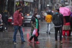 Personas en Jammu, India, protegidas con mascarilla caminan hacia un mercado en medio de la lluvia. India autorizó dos vacunas anti Covid este domingo 3 de enero de 2021 abriendo el camino a un enorme programa de inoculación contra el coronavirus.