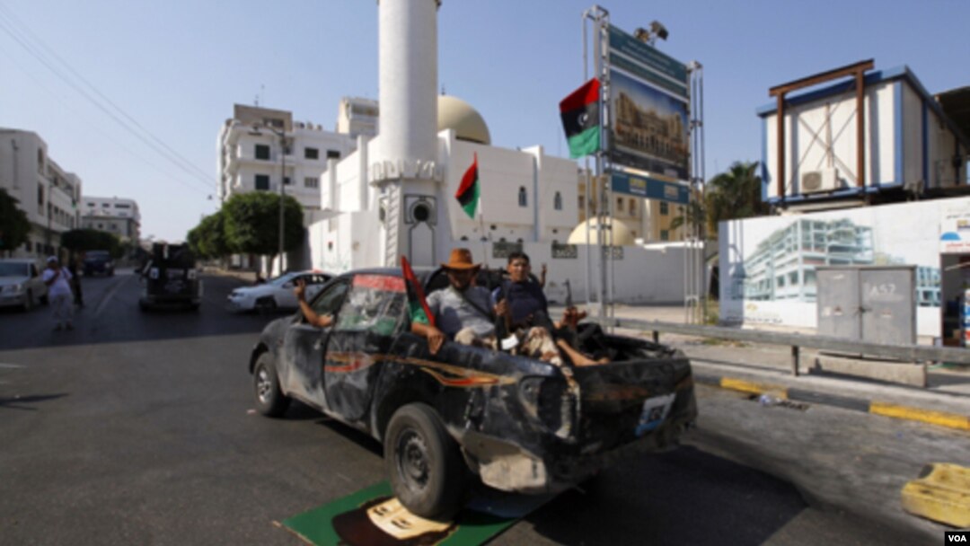Rebeldes que patrullan las calles de Trípoli pasan sobre un retrato del fugitivo Gadhafi.