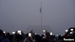 Visitors use mobile phones to take pictures and videos as they watch a flag raising ceremony at the Tiananmen Square amid heavy smog in Beijing, China.