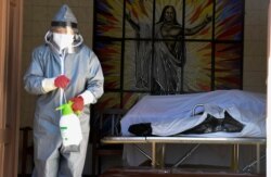 FILE - A health worker disinfects the area next to a coffin with the remains of a recently deceased resident of the San Jose nursing home in Cochabamba, Bolivia, July 16, 2020.