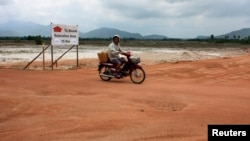 FILE - A motorcyclist rides past a dirt road at a site for a billion-dollar industrial estate in Dawei district, Myanmar, May 10, 2012. 