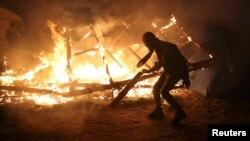 A migrant is seen in silhouette near flames from a burning makeshift shelter on the second day of the evacuation of migrants and their transfer to reception centers in France, as part of the dismantlement of the camp called the "Jungle" in Calais, France, Oct. 25, 2016.