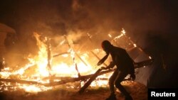 Seorang migran nampak terlihat di dekat kobaran api yang menghanguskan kamp pengungsi yang dijuluki "The Jungle" di Calais, Perancis, 25 Oktober 2016 (Foto: REUTERS/Neil Hall).