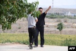 FILE - An AFP video journalist, left, is escorted away while filming at what is believed to be a reeducation camp where mostly Muslim ethnic minorities are detained, in China's northwestern Xinjiang region, June 2, 2019.