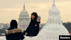 中国游客与美国国会大厦雪雕合影，背景是真实的国会大厦，上面装饰着美国当选总统唐纳德·特朗普即将就职的旗帜。(2025年1月13日)