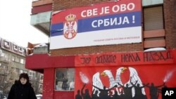 Seorang warga melewati bangunan berbendera Serbia dengan slogan 'Semuanya Milik Serbia' di kota Mitrovica, Kosovo (Foto: dok). Pertikaian antar etnis terus berlangsung di kota itu.