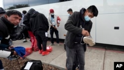 Migrants unload their items off a bus as they arrive at a bus stop after leaving a processing facility, Feb. 23, 2024, in San Diego.