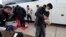 Migrants unload their items off a bus as they arrive at a bus stop after leaving a processing facility, Feb. 23, 2024, in San Diego.