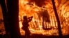 FILE - A firefighter sprays water as flames from the Camp Fire consume a home in Magalia, Calif., Nov. 9, 2018. A new federal report warns that extreme weather disasters are worsening in the U.S. The report, issued Nov. 23, also frequently contradicts President Donald Trump.