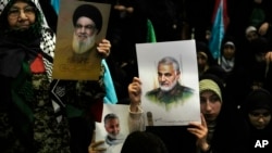 Warga mengangkat poster mendiang komandan Pasukan Garda Revolusi Iran, Jenderal Qassem Soleimani, kanan dan poster pemimpin Hizbullah yang terbunuh Hassan Nasrallah, selama upacara peringatan kematian Soleimani di Masjid Agung Imam Khomeini di Teheran, Kamis, 2 Januari 2025.