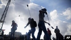 FILE - Palestinian protesters use slingshots to throw stones towards Israeli security forces during clashes following a protest marking the 11th anniversary of the death of late Palestinian leader Yasser Arafat, in the West Bank city of Ramallah, Wednesda