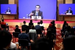 Chinese Premier Li Keqiang is seen on screens during a press conference held via online video link following the National People's Congress at the Great Hall of the People in Beijing on May 28, 2020.