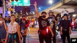 Sekelompok kecil pengunjuk rasa pro-demokrasi memberi hormat tiga jari kepada petugas polisi anti huru hara di dekat Gedung Pemerintah di Bangkok, Thailand, Kamis, 15 Oktober 2020. (Foto: AP)