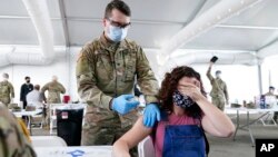 FILE - A woman covers her eyes to avoid seeing the needle while she receives the Pfizer COVID-19 vaccine at a FEMA vaccination center at Miami Dade College in Miami, April 5, 2021.