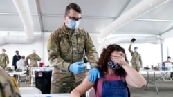 FILE - A woman covers her eyes to avoid seeing the needle while she receives the Pfizer COVID-19 vaccine at a FEMA vaccination center at Miami Dade College in Miami, April 5, 2021.