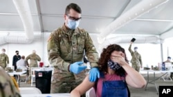 FILE - A woman covers her eyes to avoid seeing the needle while she receives the Pfizer COVID-19 vaccine at a FEMA vaccination center at Miami Dade College in Miami, April 5, 2021.