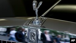 FILE - Pedestrians are reflected in the chrome work under the Spirit of Ecstasy on the front of a Rolls- Royce luxury automobile, in a show room in London, July 8, 2014.