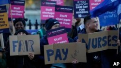 FILE - Demonstrators hold up placards in support of a strike by nurses outside St Thomas' Hospital in London, Dec. 20, 2022. 