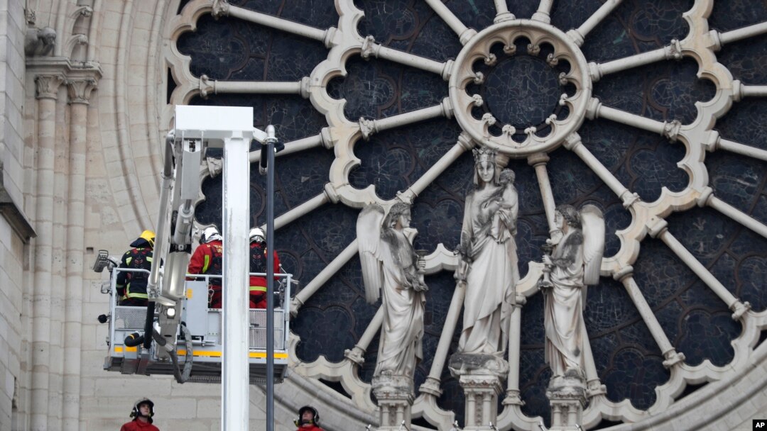 Para petugas kebakaran di dekat jendela berbentuk bunga mawar di Katedral Notre Dame, Paris, Perancis, 16 April 2019.