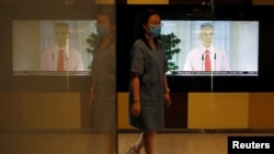 Seorang perempuan dengan masker wajah berjalan melewati layar yang menunjukkan siaran Perdana Menteri Singapura Lee Hsien Loong membahas wabah Covid-19, di kawasan pusat bisnis di Singapura, 3 April 2020. (Foto: REUTERS)