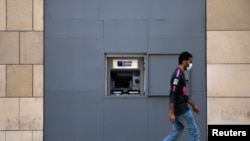 FILE - A man wearing a face mask walks past a fortified Blom Bank ATM, in Beirut, Lebanon, Aug. 21, 2020. 