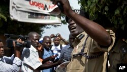 A Ugandan policeman holds up a newspaper, just before police fired tear gas to disperse the demonstration in downtown Kampala, Uganda, May 28, 2013. Some local activists are writing and distributing books that they hope can be as effective as placards.