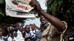 Un policier ougandais tient un journal devant des journalistes et membres du Réseau des droits de l'homme qui protestent devant le siège du journal Daily Monitor, à Kampala, Ouganda, 3 mai 2013.