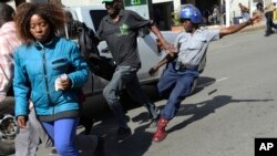 FILE: A riot police man kicks out at a man during protests in Harare, Friday, Aug. 16, 2019. 