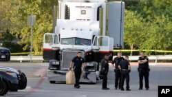 San Antonio police officers investigate the scene Sunday, July 23, 2017, where eight people were found dead in a tractor-trailer loaded with at least 30 others outside a Walmart store in stifling summer heat in what police are calling a horrific human tra